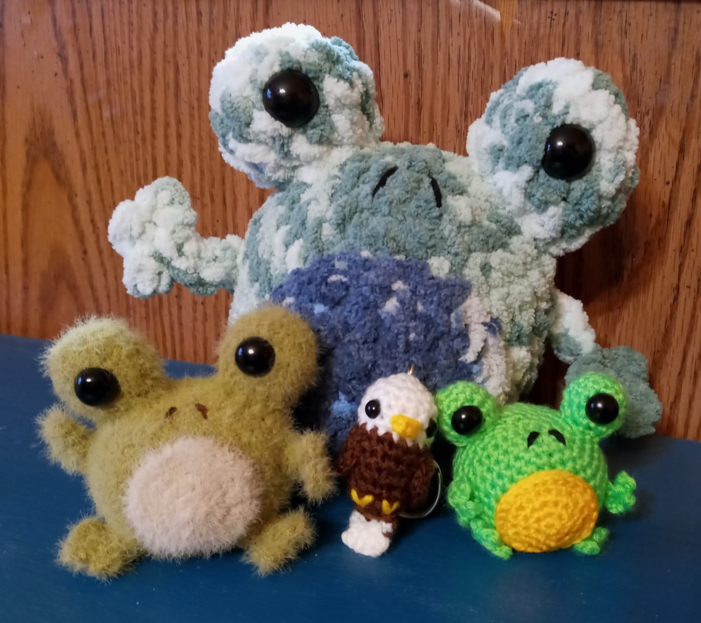 Three crochet frogs of varying sizes with a tiny crochet eagle in the middle